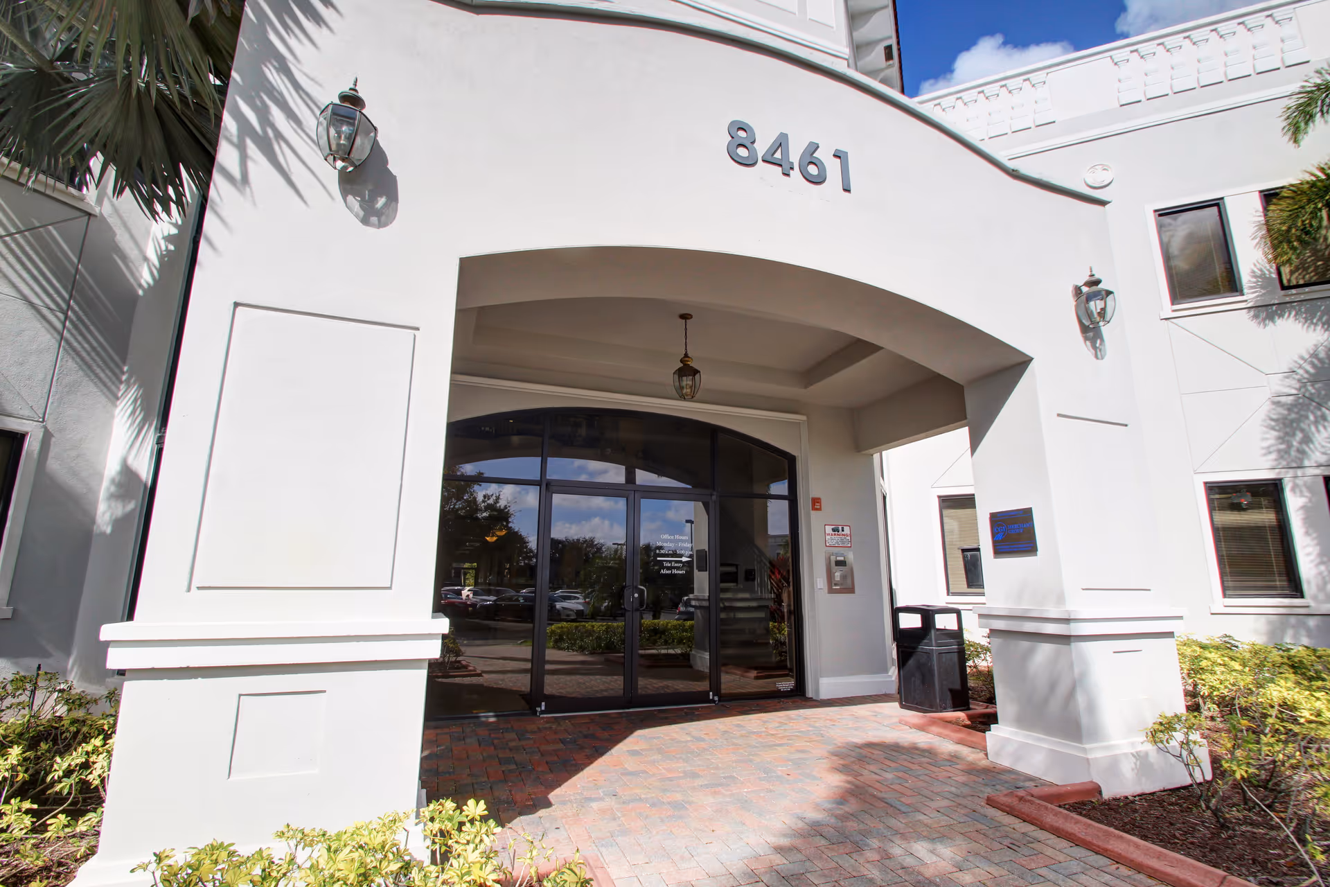 White building entrance with arched doorway, glass doors, and 8461 on facade.