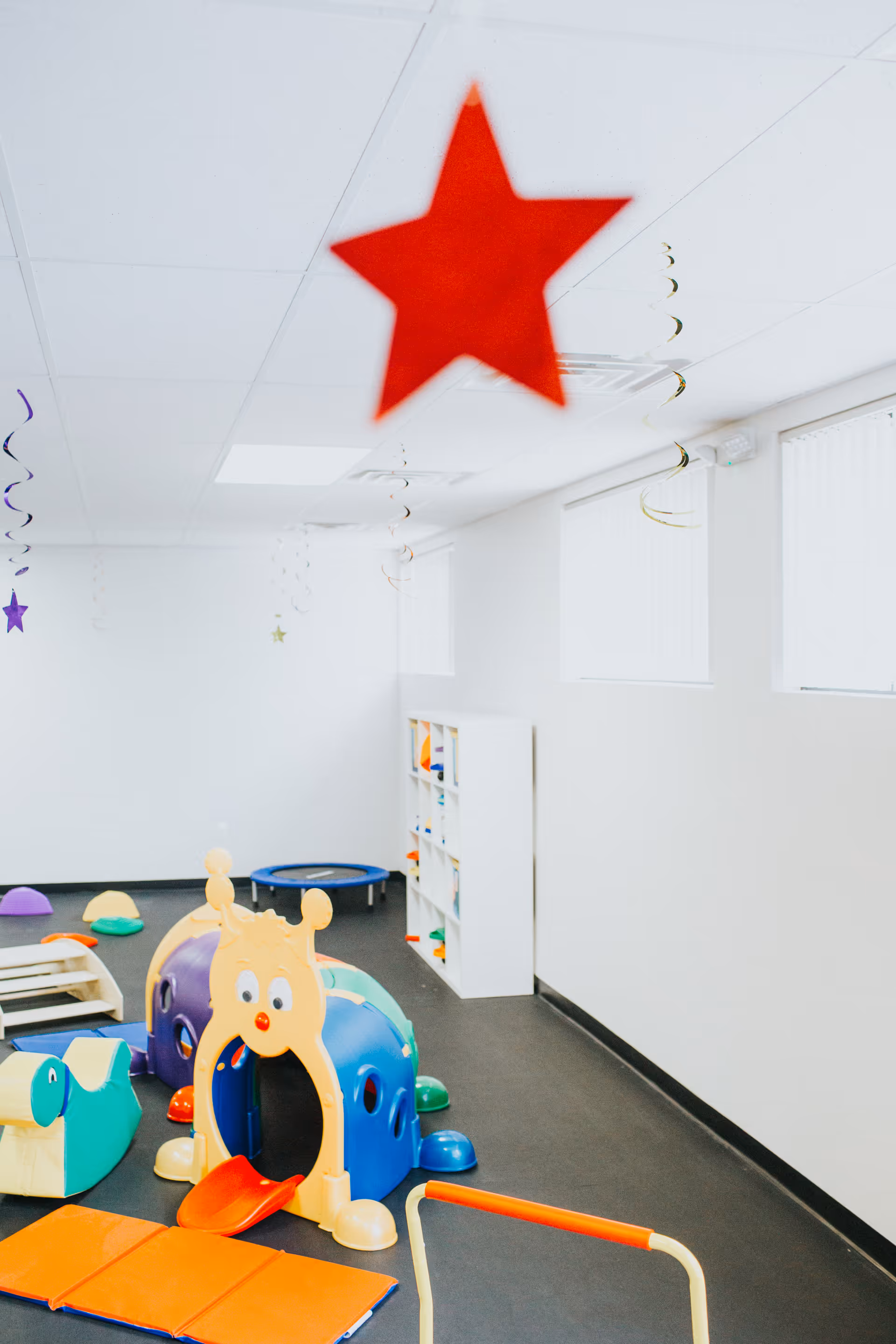 Bright playroom with colorful plastic toys, shelves, and hanging star decorations.