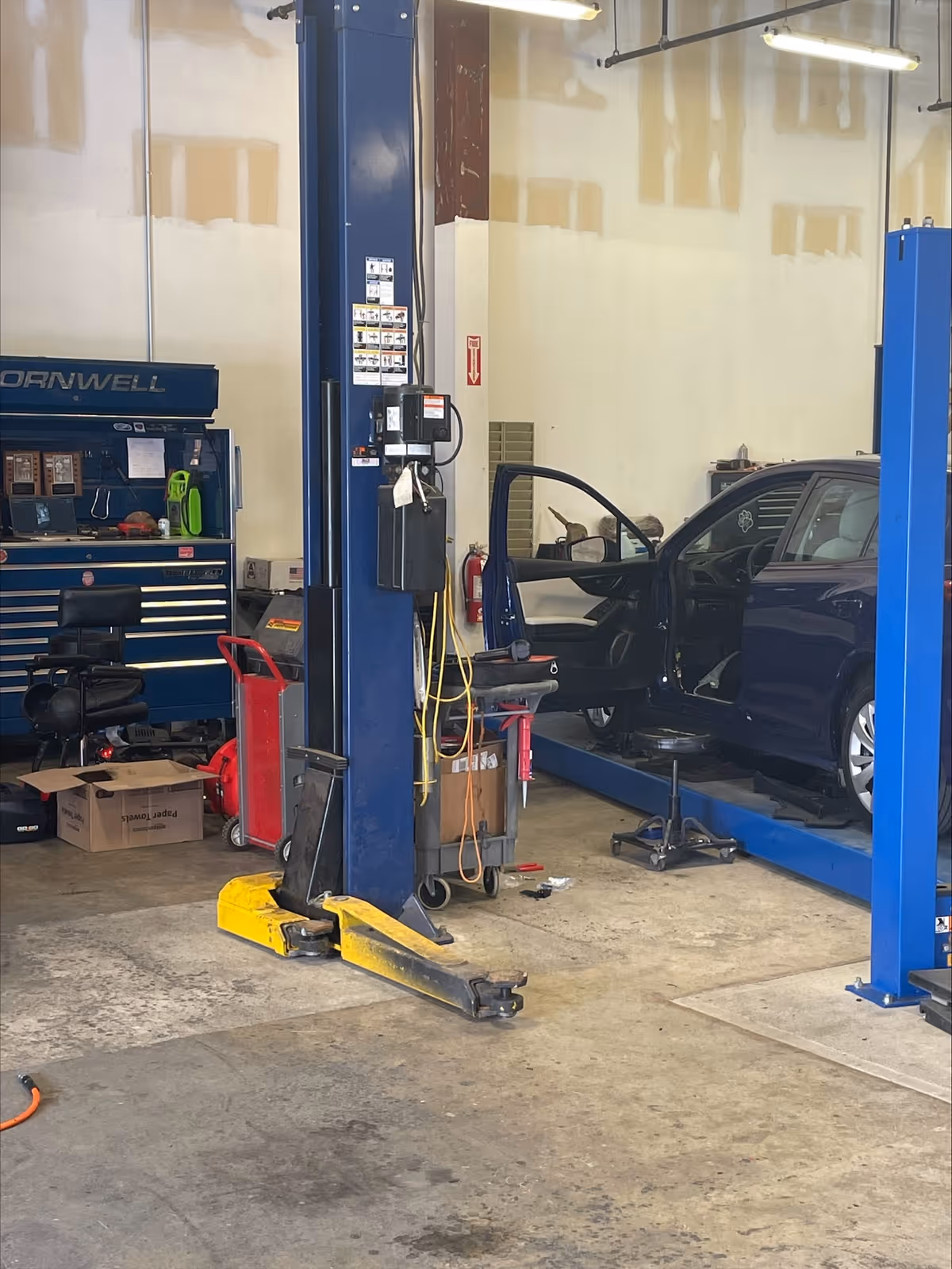 Blue car on a lift inside a workshop with tools and equipment.
