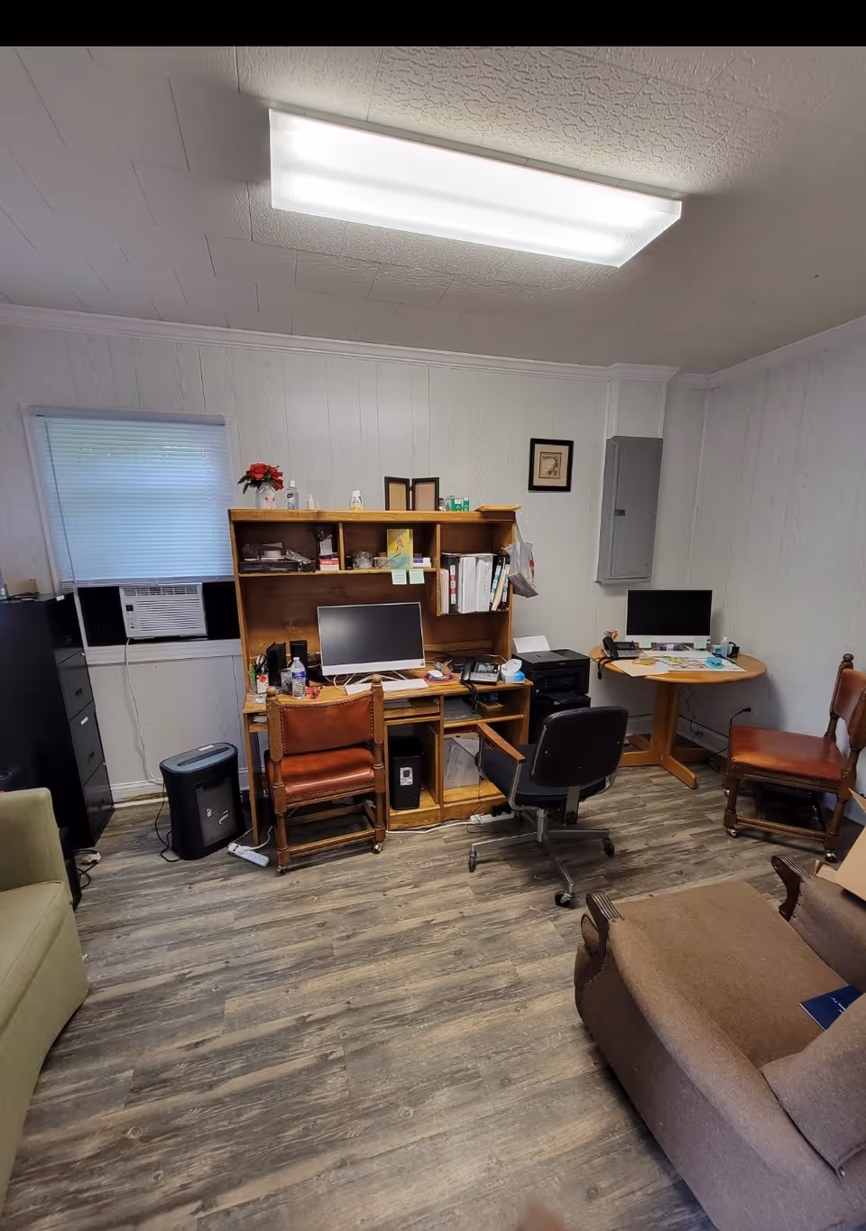 A small office area with desks, computers, shelves, and chairs in a senior living facility.