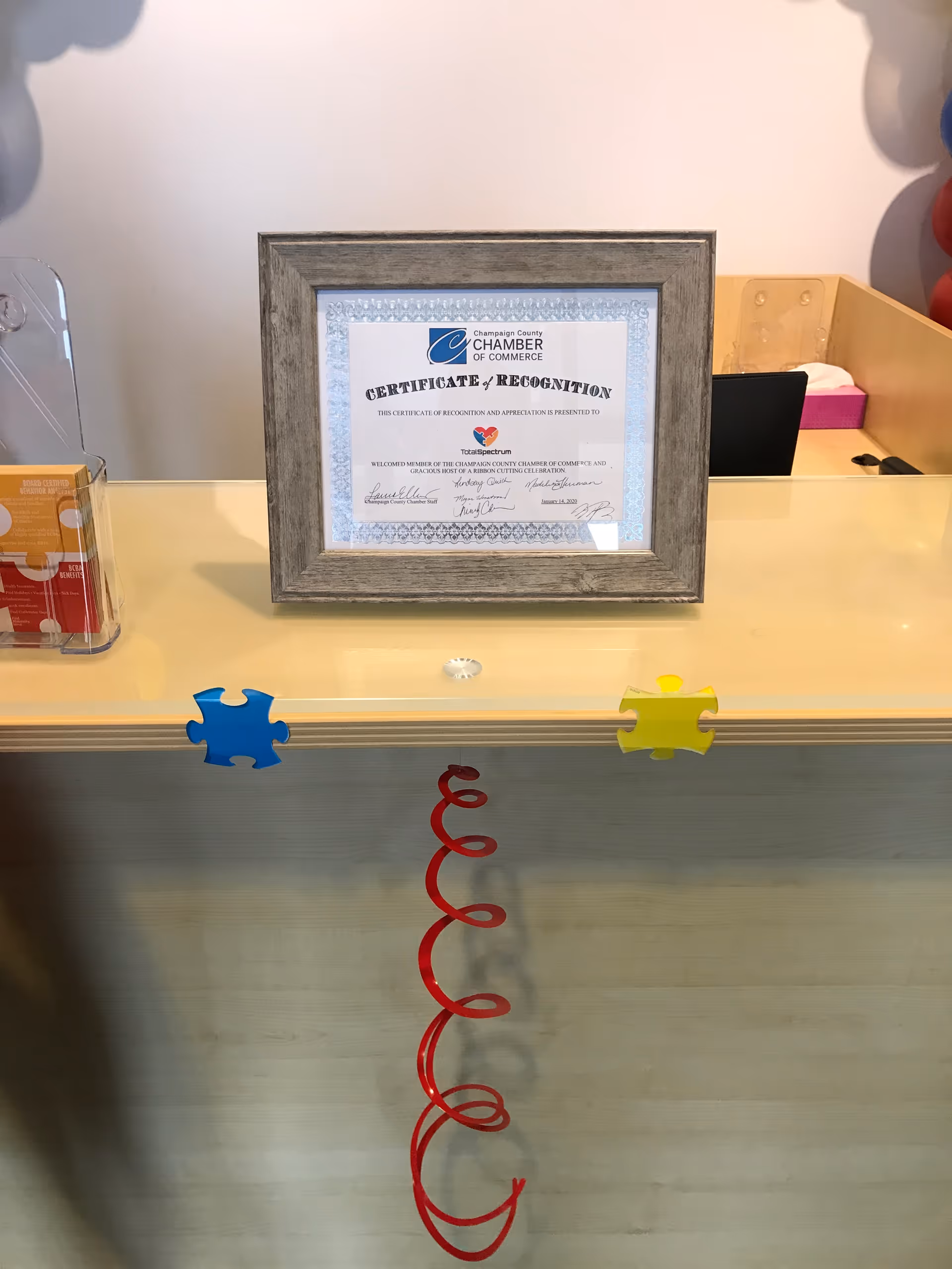 Framed certificate on a reception desk with puzzle pieces and a red spiral decoration.