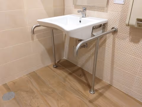 White wall-mounted sink with metal grab bars in an accessible bathroom.