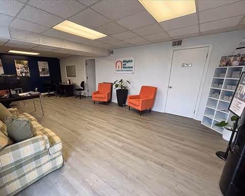 Lobby seating area with orange chairs, couch, plants, and Right at Home sign.