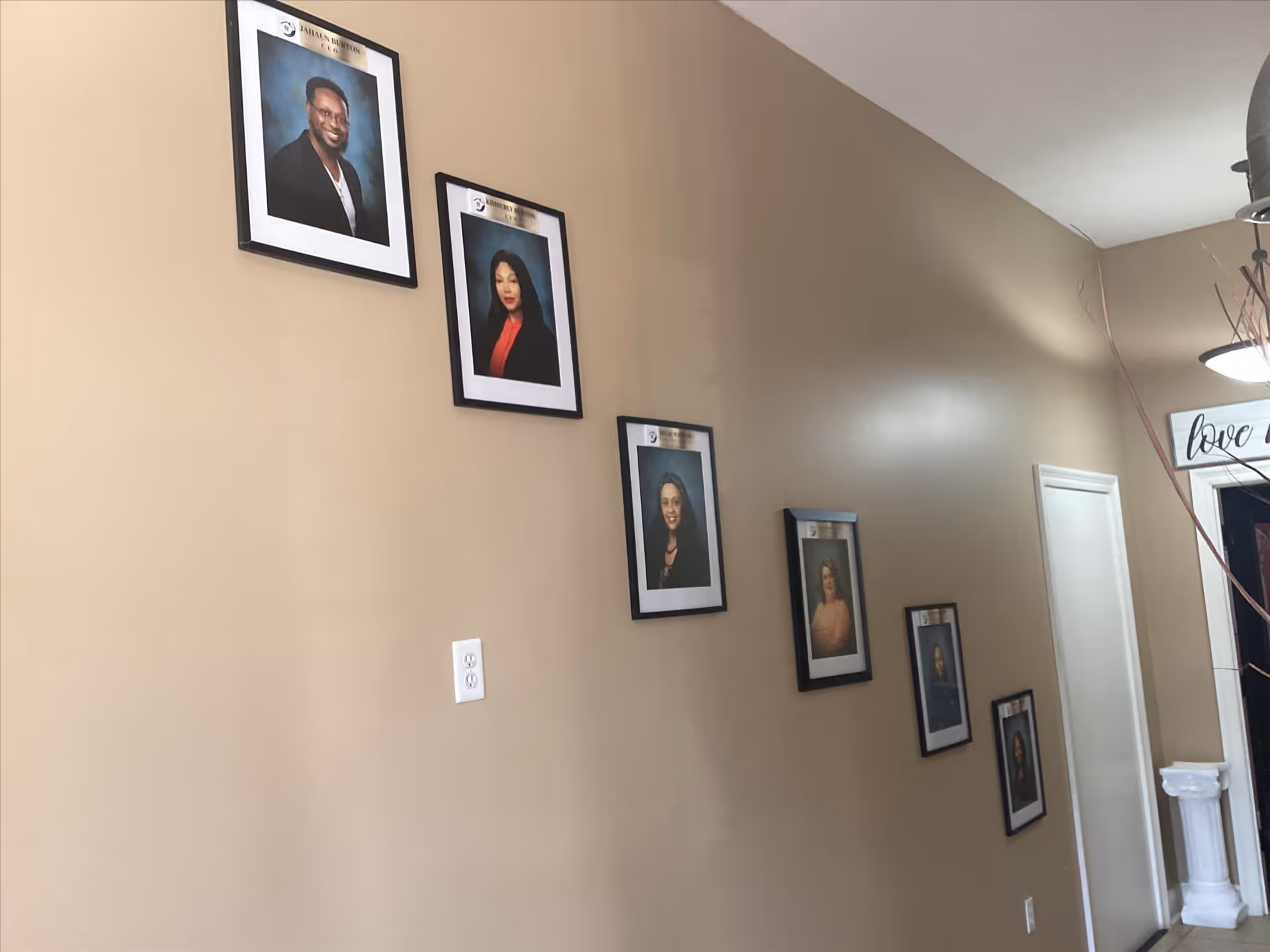 Beige hallway in a senior living facility featuring framed portraits along the wall.