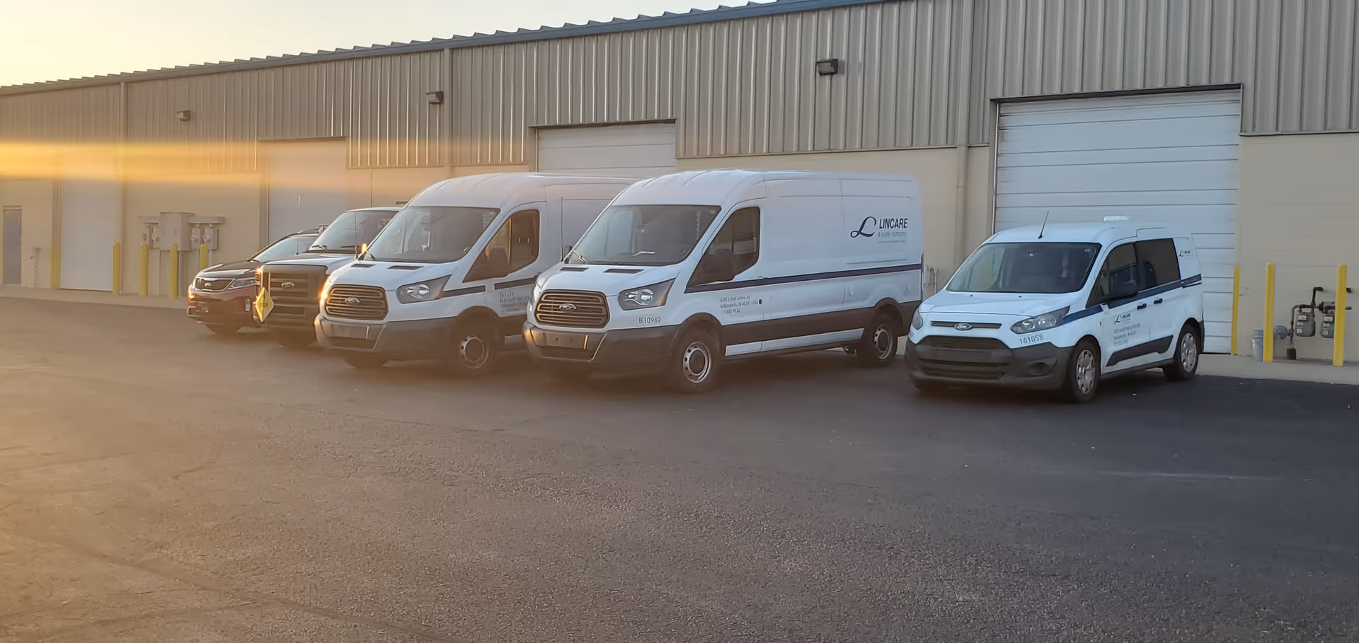 Several white LINCARE vans parked in front of a beige industrial building.