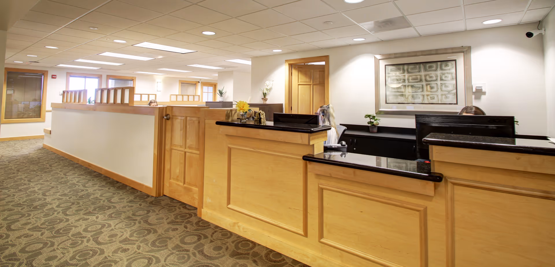 Interior view of a senior living facility reception desk with wood paneling and patterned carpet.
