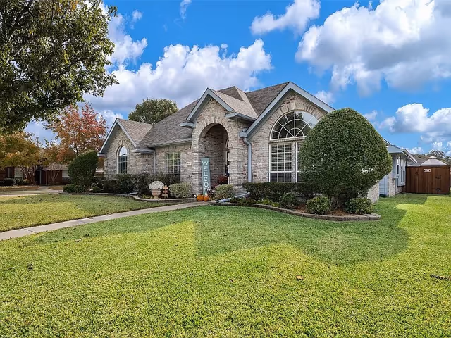 Front exterior of a brick building with arched entry, trimmed shrubs, and a wide green lawn.