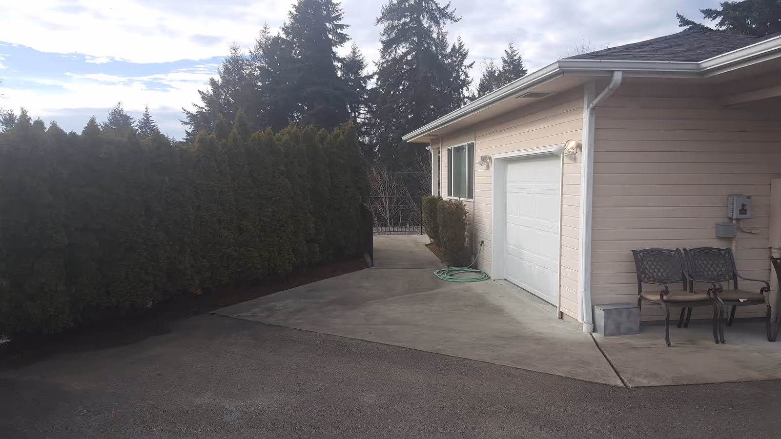 Exterior view of a beige building with a white garage door, concrete driveway, and seating.