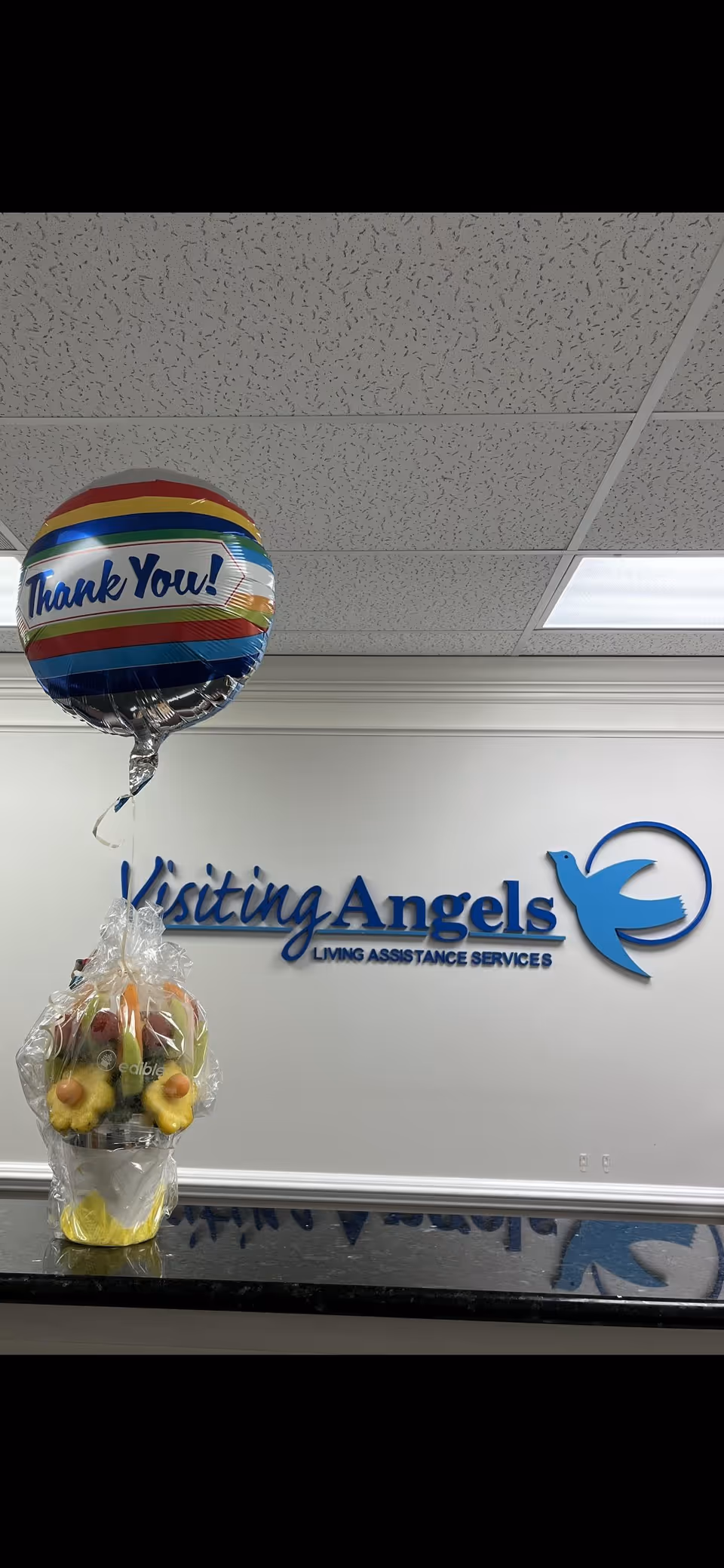 Interior reception area with Visiting Angels sign, balloon, and fruit basket on counter.