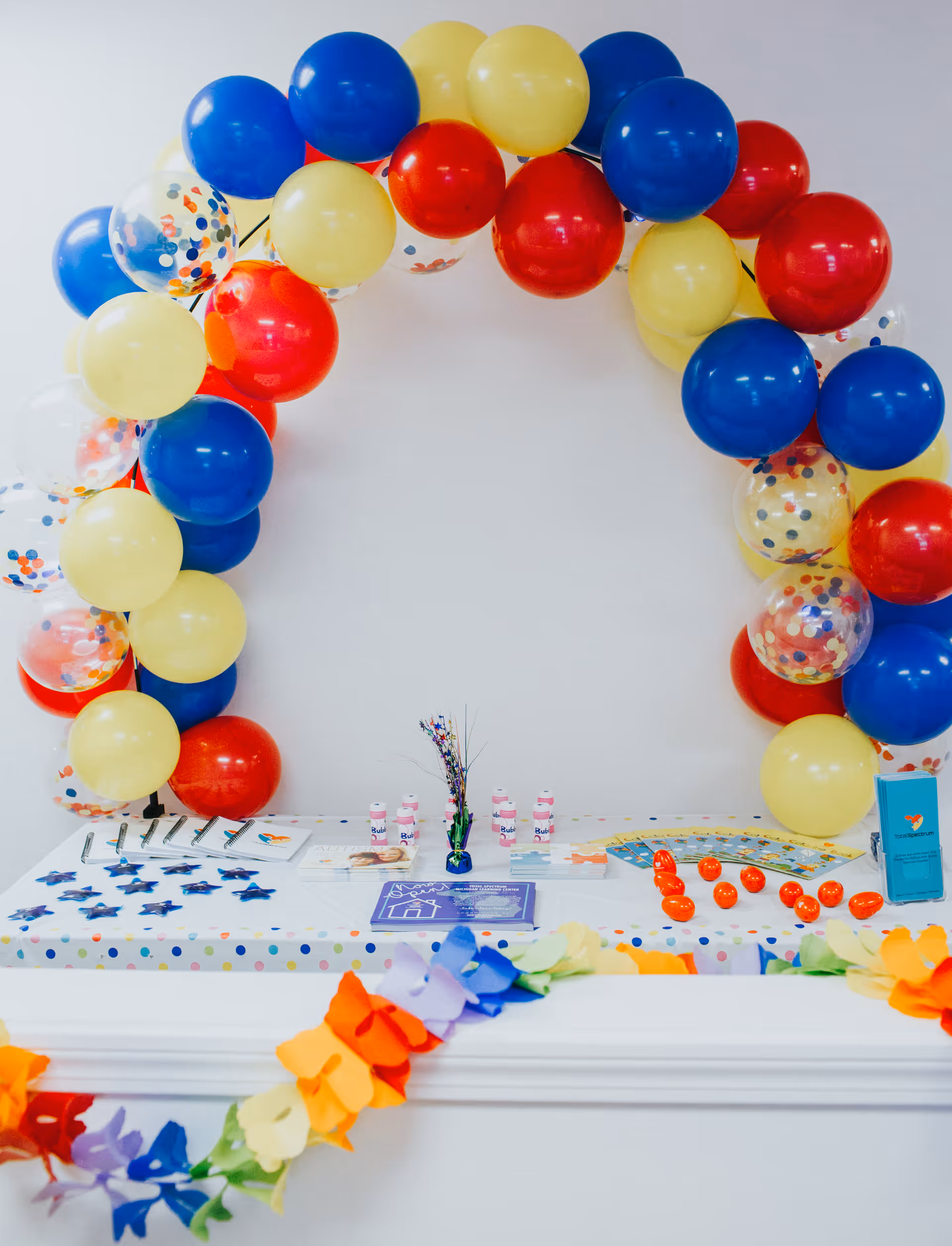 Colorful balloon arch frames a celebratory table in a bright, white interior room.