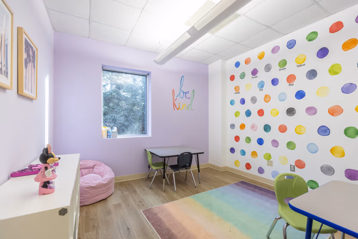 Colorful therapy room with lavender walls, polka-dot mural, and child-sized tables and chairs.