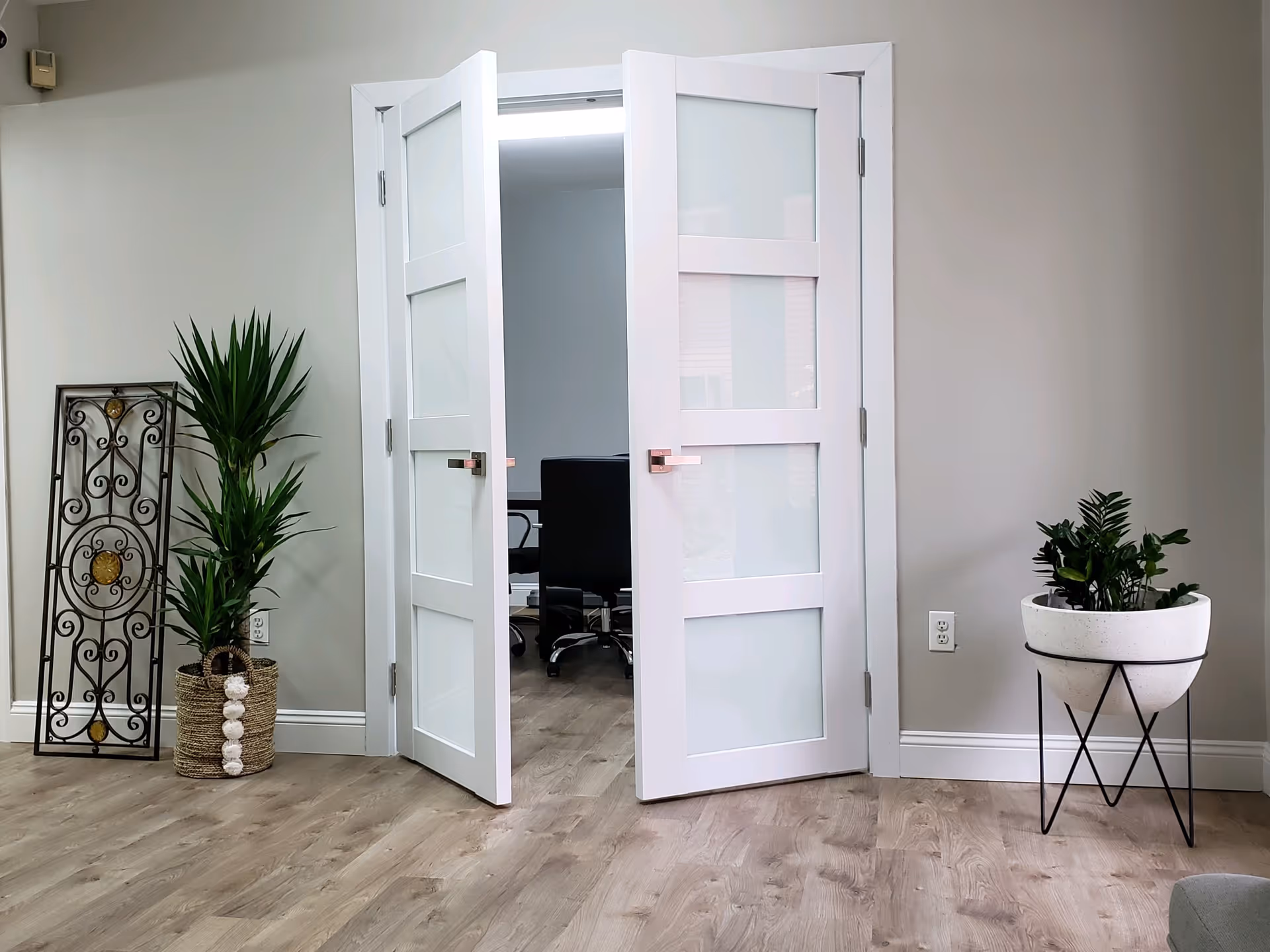 Double glass doors open to a bright office area with chairs and plants.