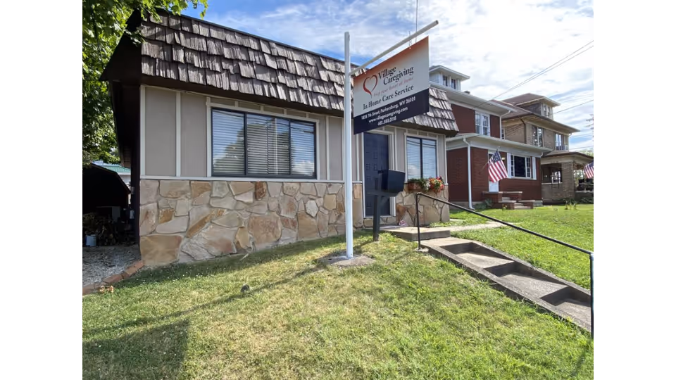 Small building with stone base, sign, steps, and lawn in front of Village Caregiving.