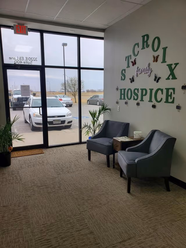 Interior hospice lobby with two chairs, a small table, plants, and wall sign.