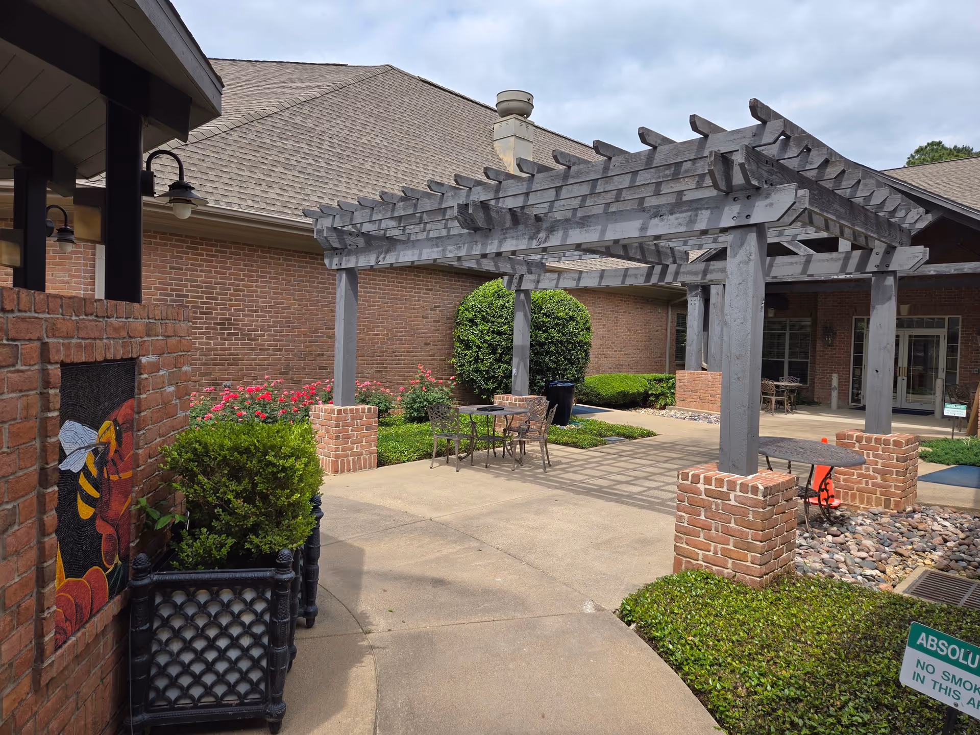 Outdoor courtyard of hospice facility featuring brick walls, pergola, and metal seating.