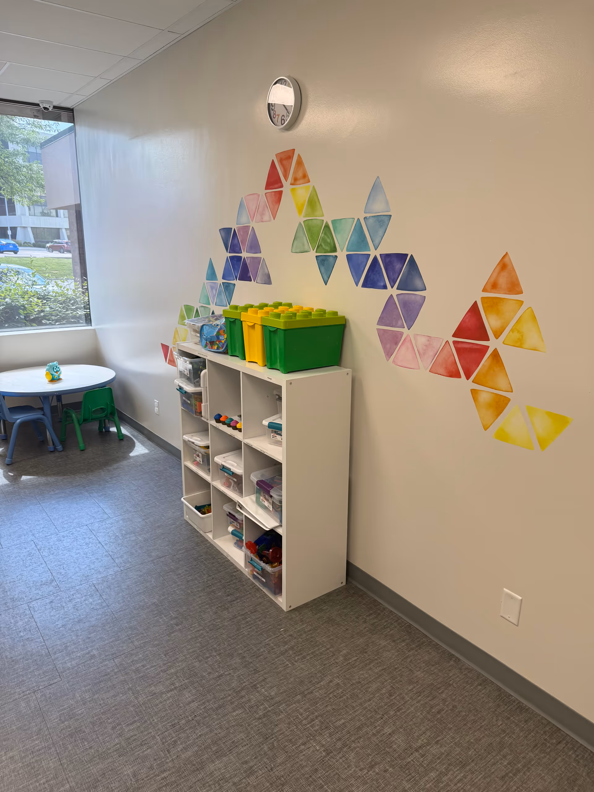 Interior play area with cubby storage, colorful wall triangles, and small table.