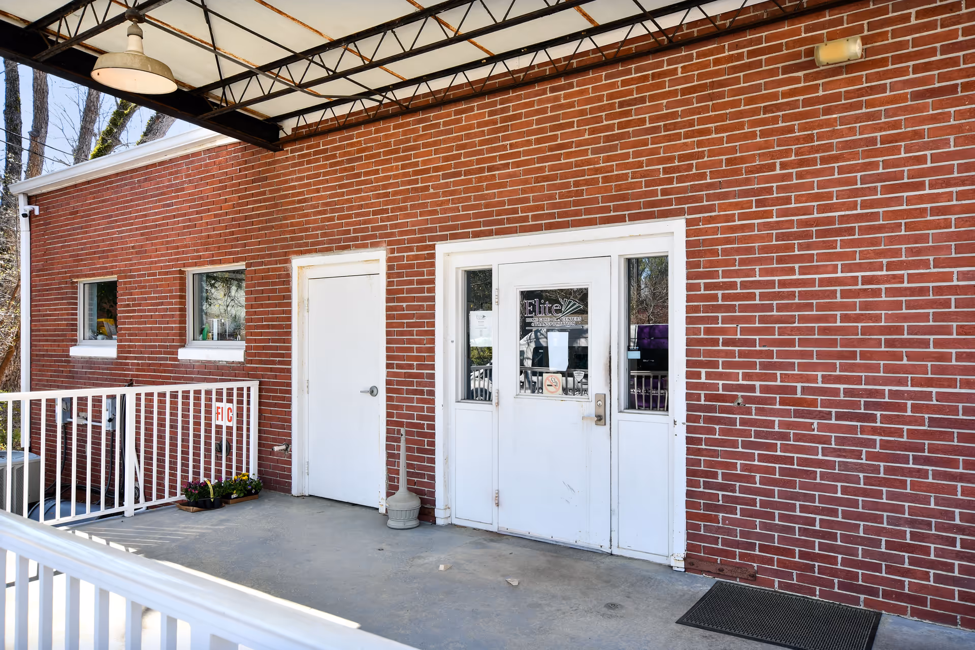 Brick facility exterior with white doors labeled Elite, railing, and a covered entrance.