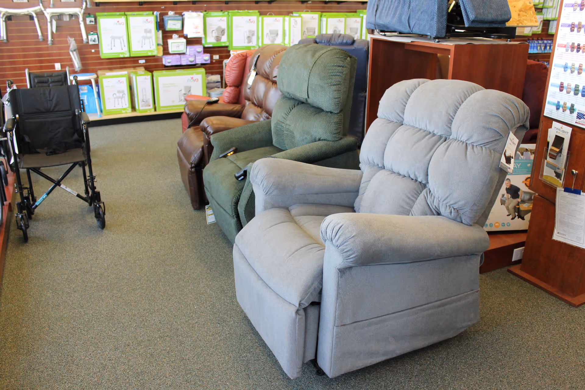 Wheelchairs and plush recliners on display in a showroom with boxed supplies along the walls.