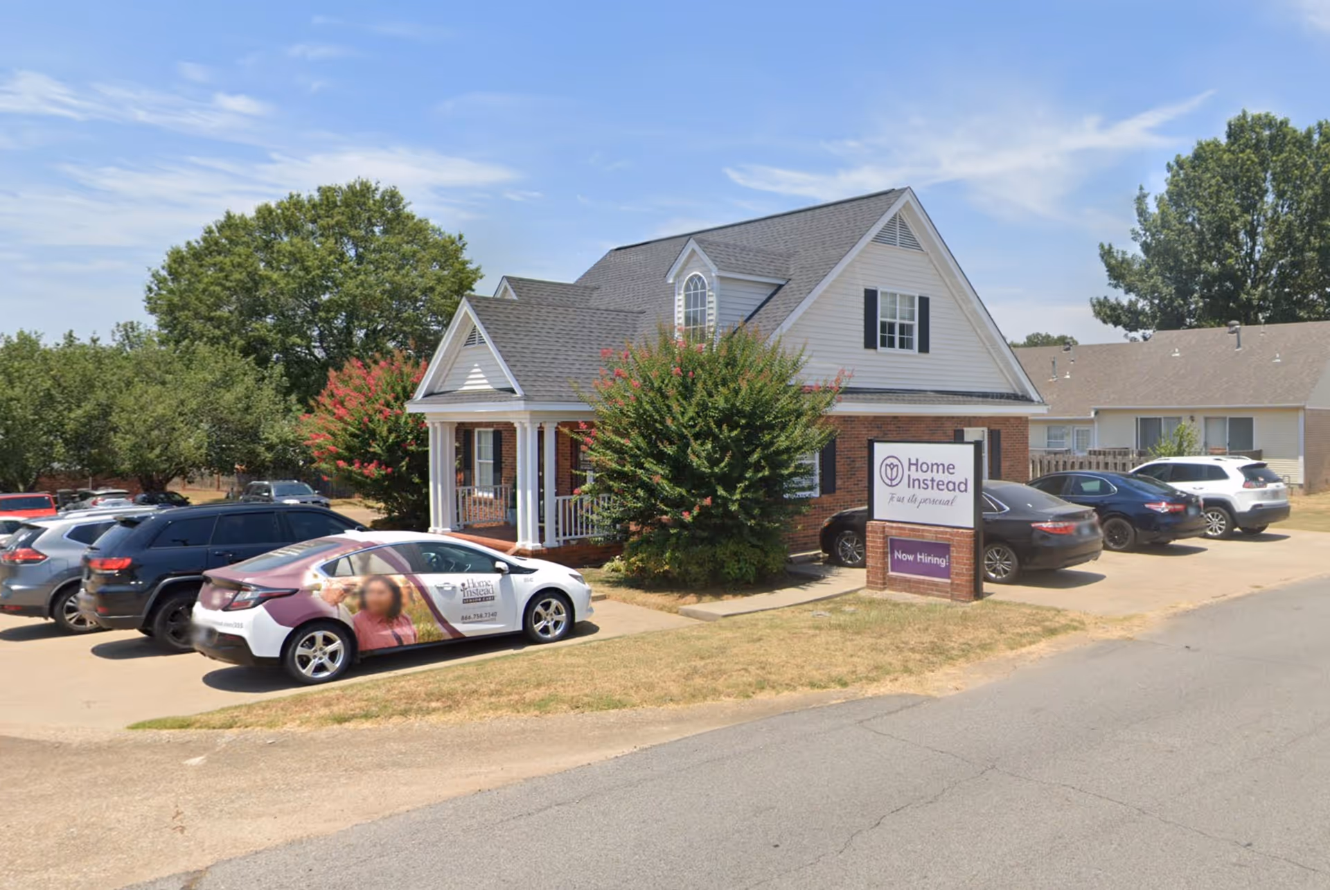 Front view of a two-story Home Instead senior care facility with parked cars