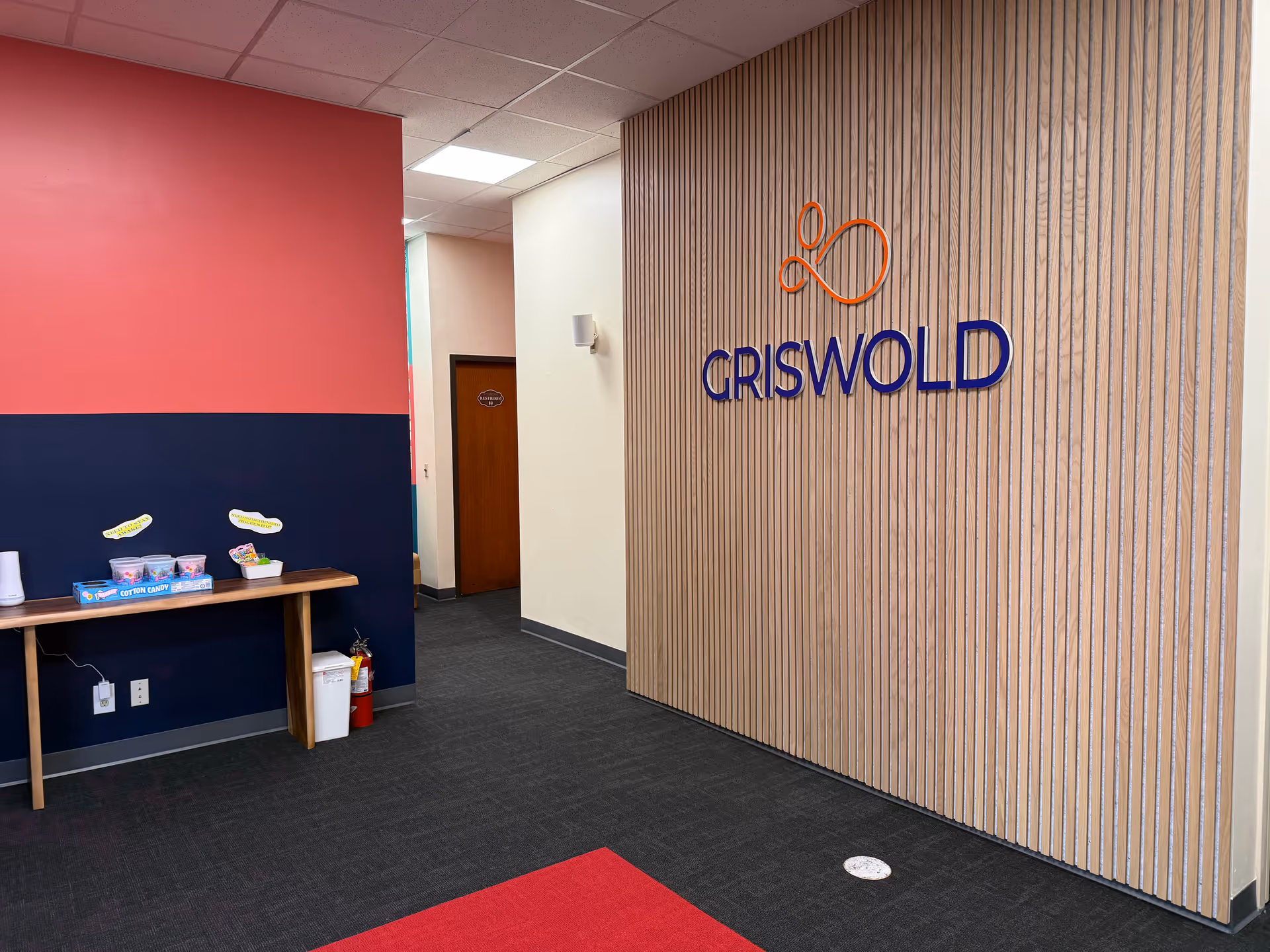Interior hallway with pink and navy walls, a snack table, and Griswold sign.