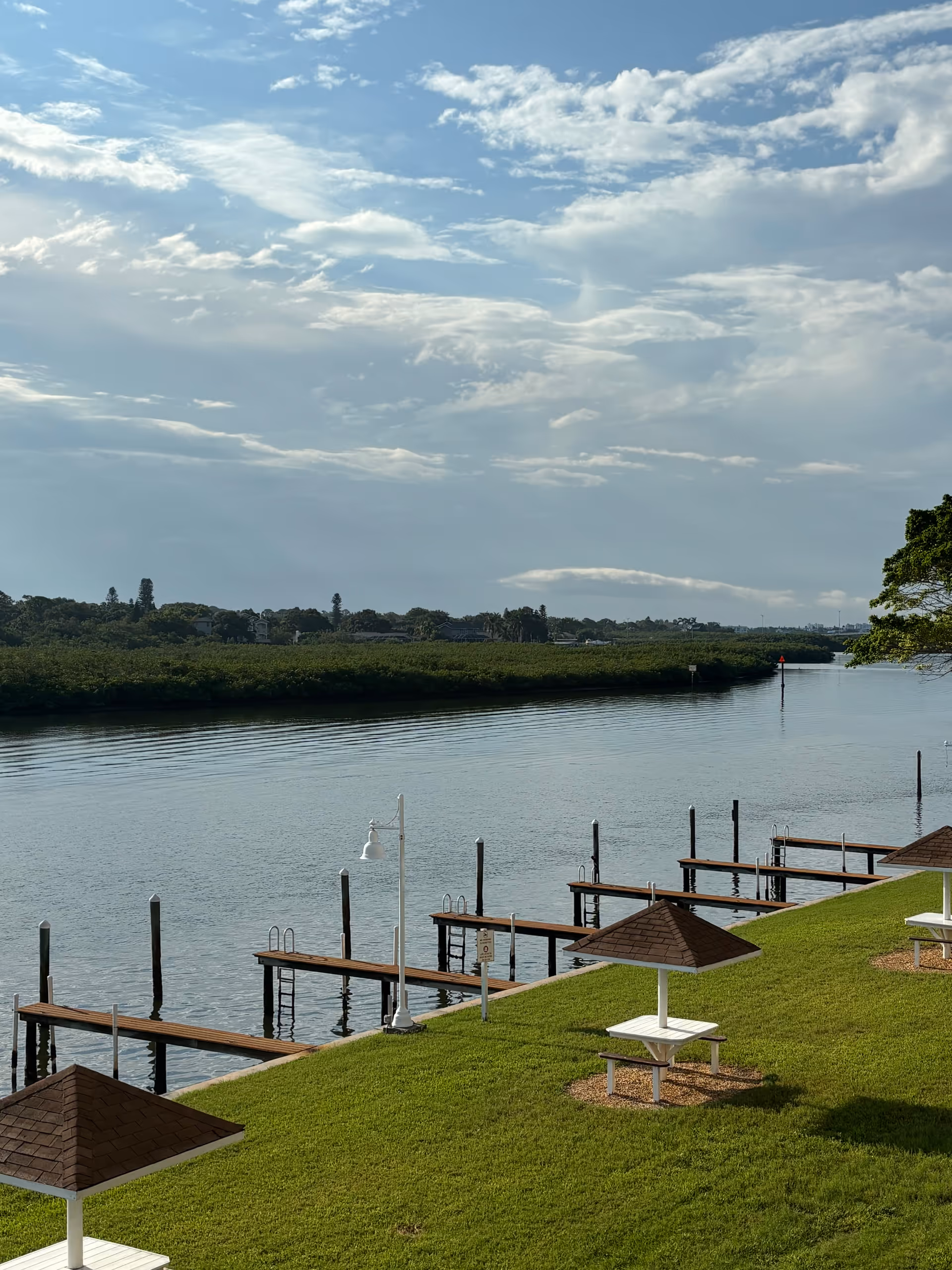 River view with wooden docks along a grassy bank and white gazebo shelters under blue sky.
