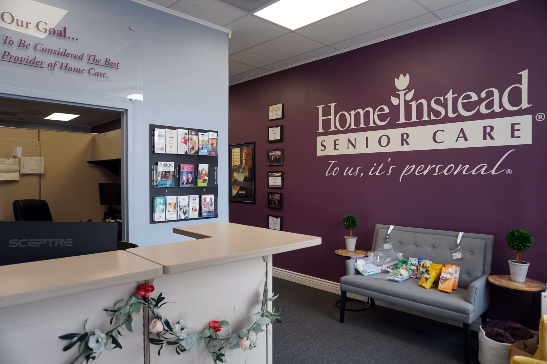 Reception area with purple wall branding, a desk, and a sofa with snacks.