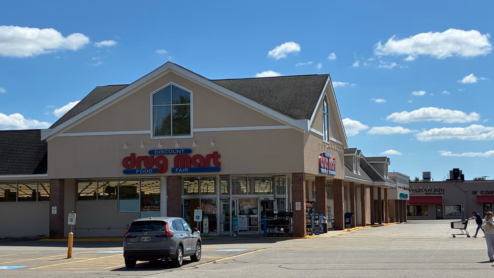 Front of Discount Drug Mart storefront in a strip mall with blue sky
