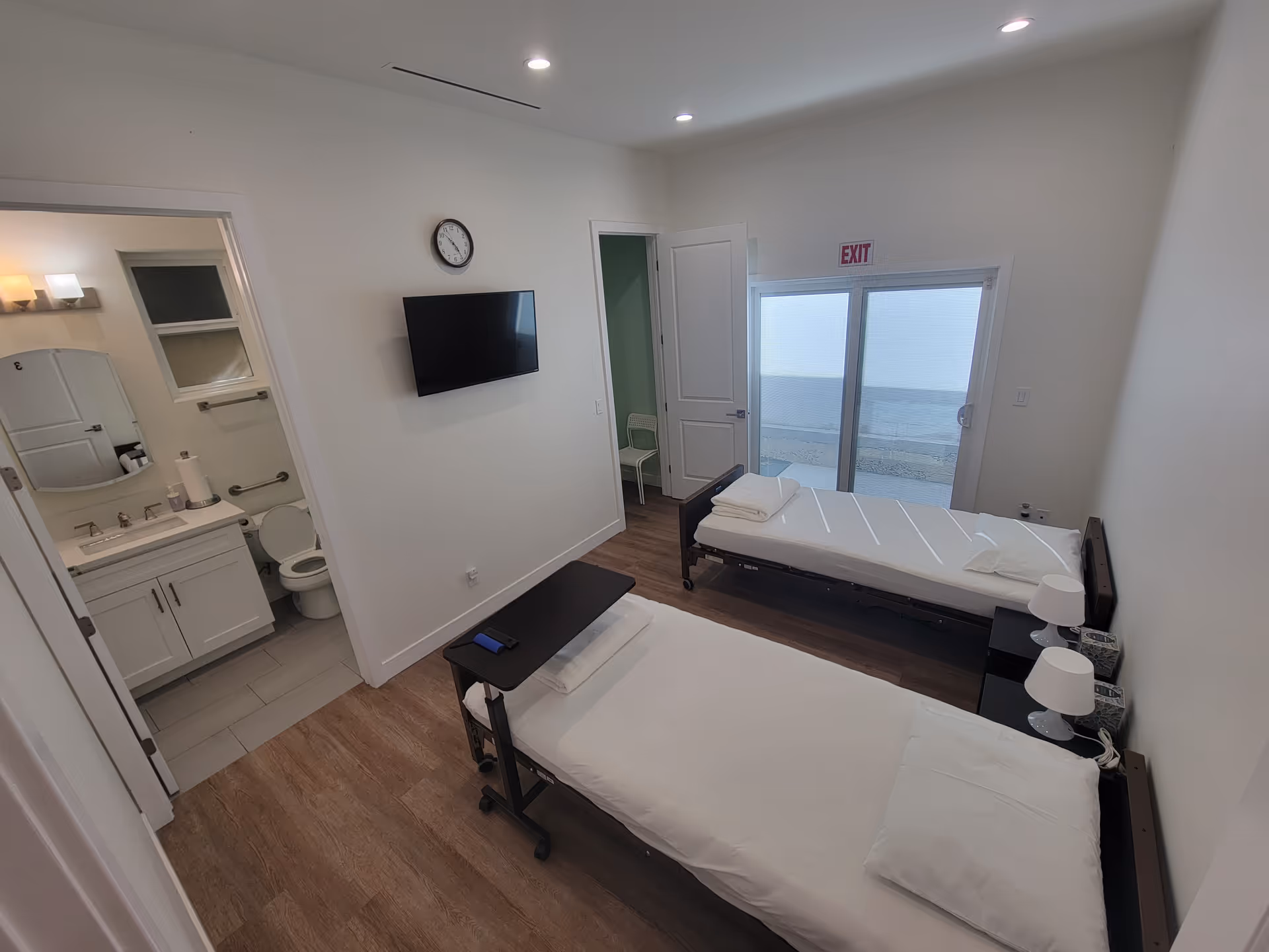 Two single beds in a bright, modern bedroom with glass doors to an outdoor water view.