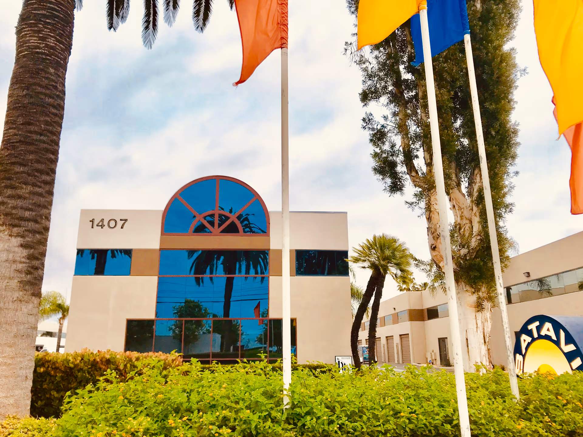 Exterior view of a modern facility with blue glass, palm trees, and flagpoles.