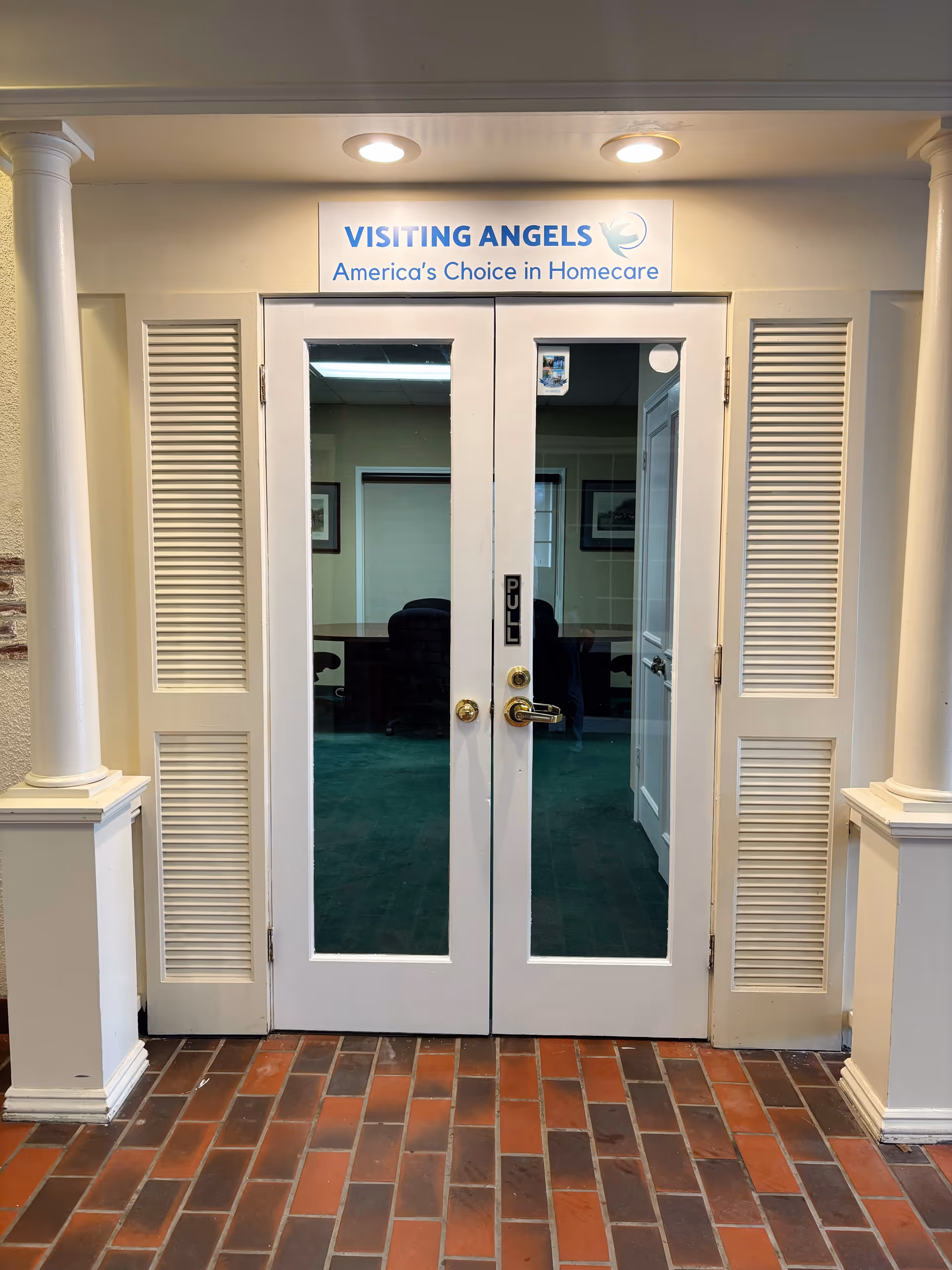 Double glass doors bearing the Visiting Angels sign open into a brick-floor interior lobby.
