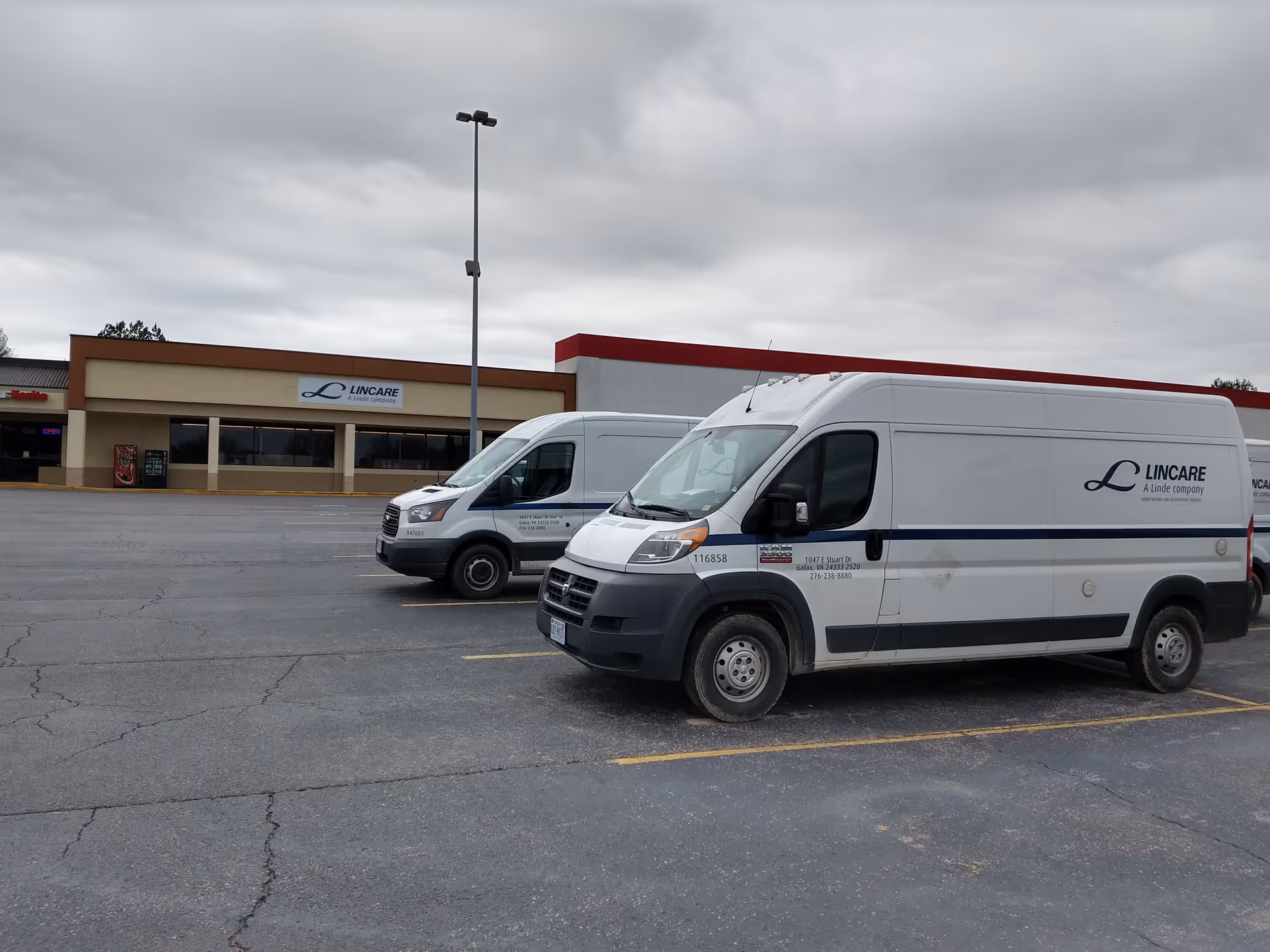 Two white LINCARE vans parked in a lot in front of the facility.
