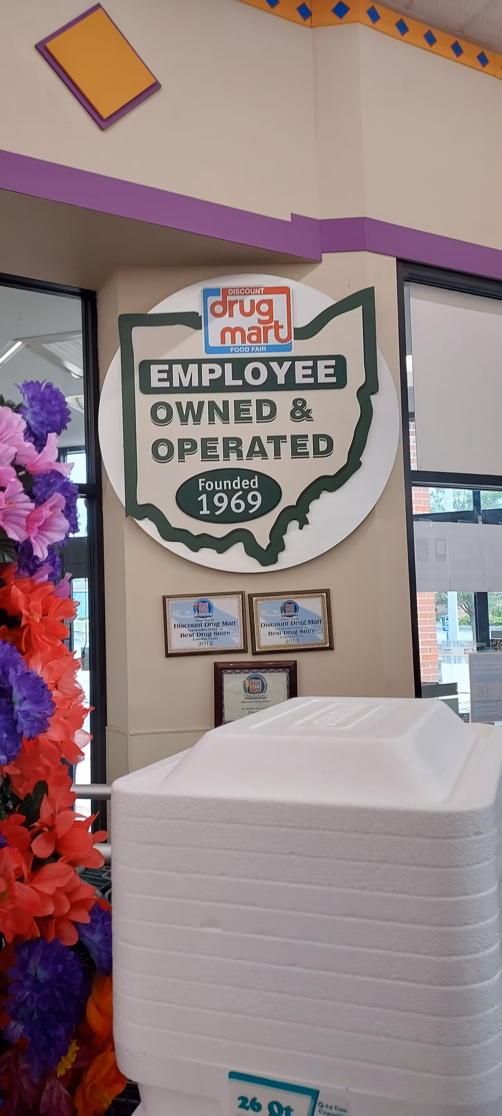 Indoor facility lobby featuring a Discount Drug Mart sign, wall plaques, and a white cooler.