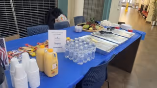 Blue table with buffet food, drinks, and disposable dishes set in a hallway dining area.