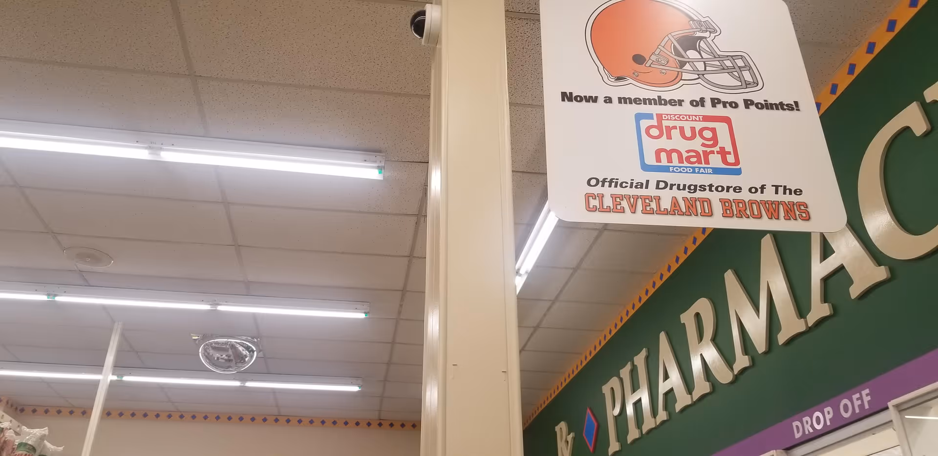 Interior of Discount Drug Mart with fluorescent ceiling lights and a large green pharmacy sign.
