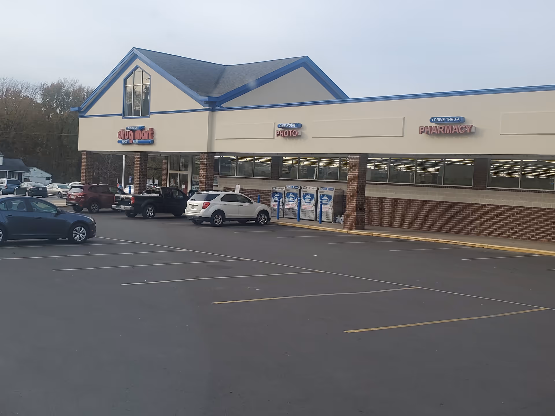 Exterior view of a Discount Drug Mart storefront with parked cars.