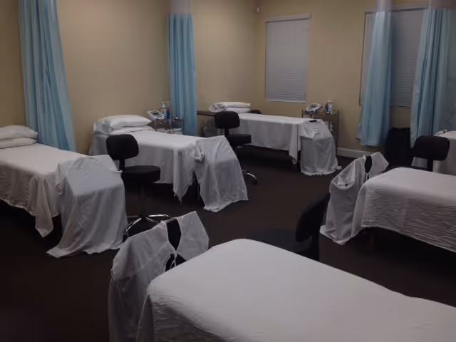 Several treatment beds with white sheets and blue curtains in a clinic-style therapy room