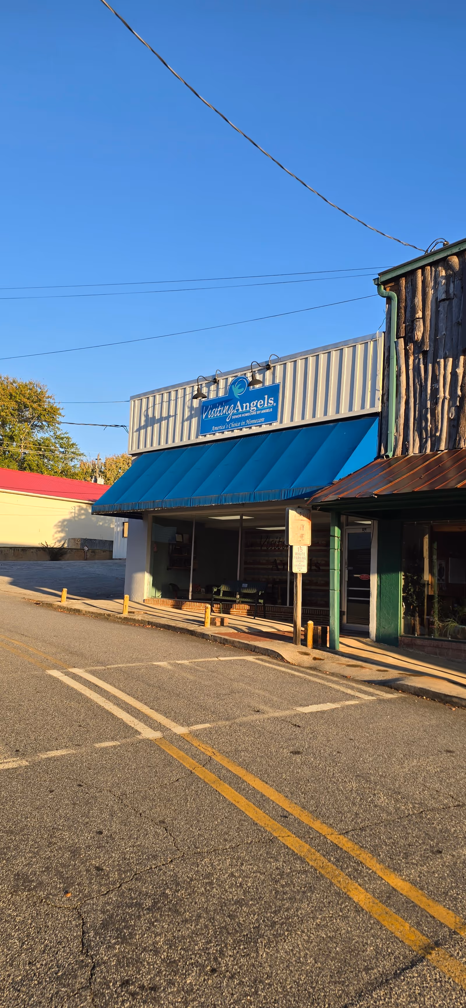 Exterior storefront for Visiting Angels Senior Home Care with blue awning along empty street.