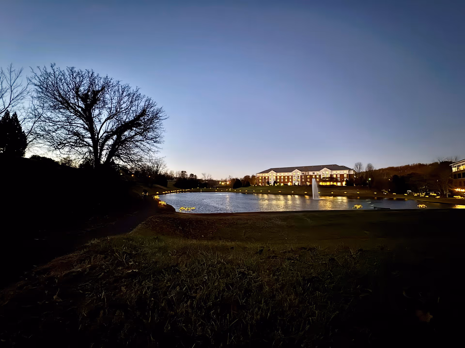 Evening exterior view of Hospice of the Piedmont campus with a pond and fountain.