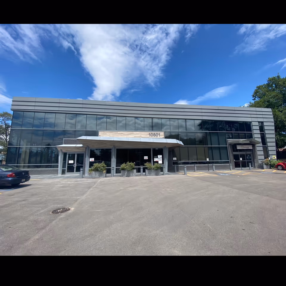 Exterior view of Healthcare Plus Caregivers facility with glass frontage, entrance canopy, and parking lot.