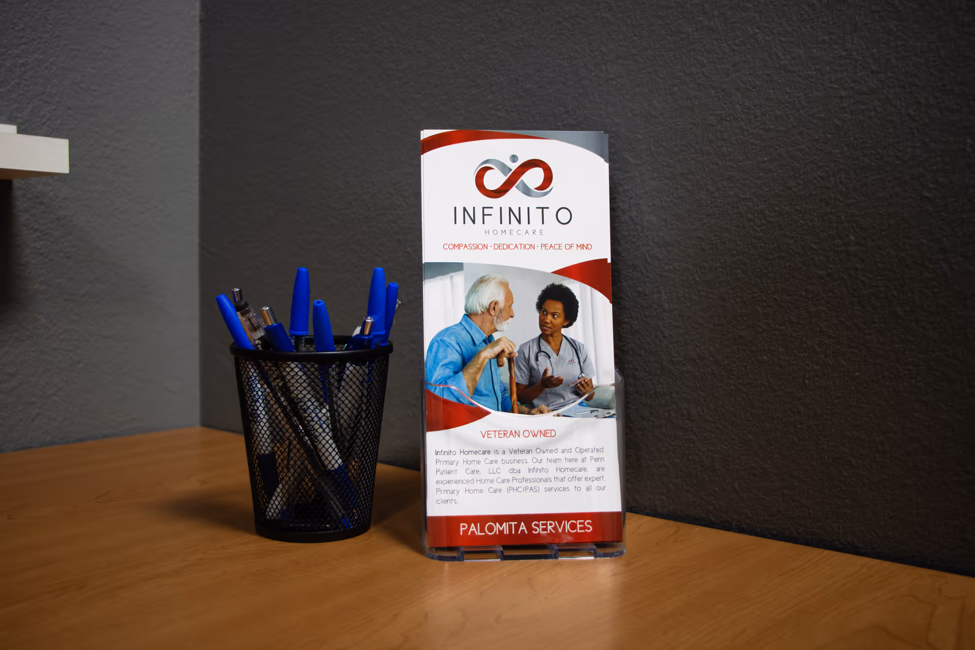 A brochure for Infinito Homecare sits on a wooden desk beside a blue pen cup.