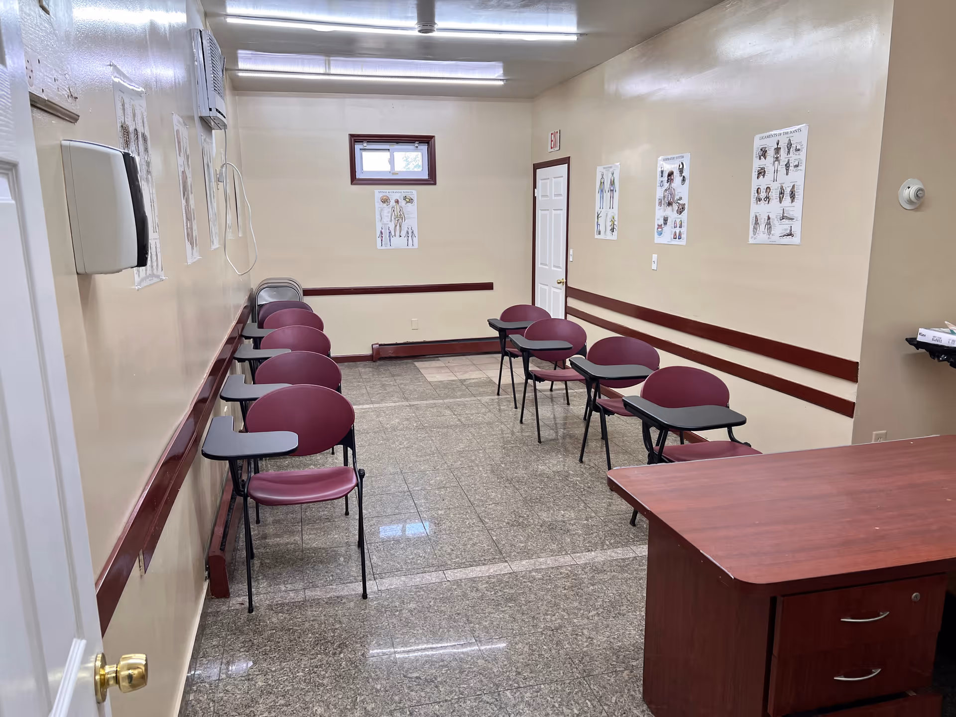 A small beige-walled waiting area with maroon chairs and attached desks along walls.