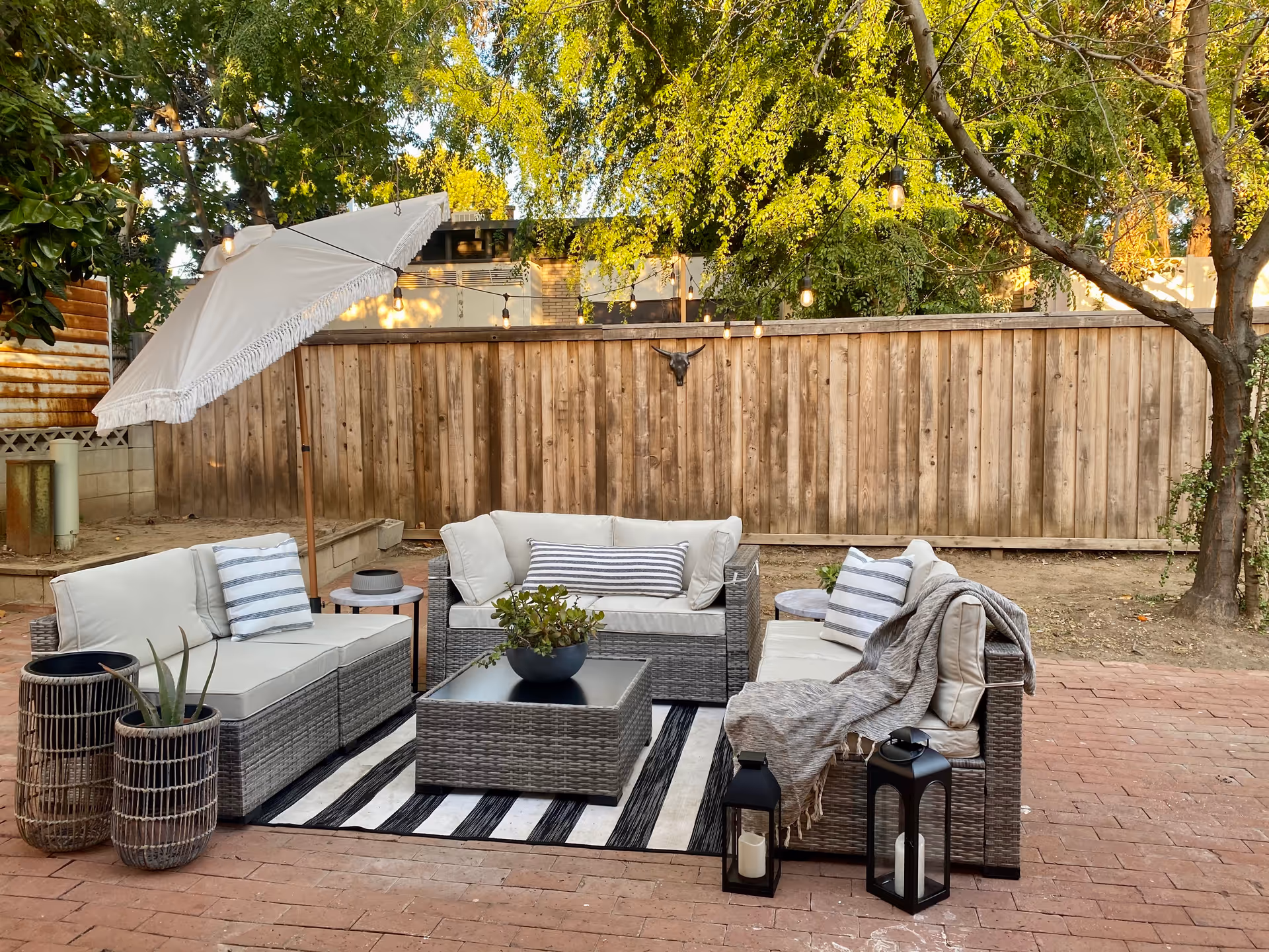 Outdoor patio with wicker seating, umbrella, string lights, and a wooden fence.