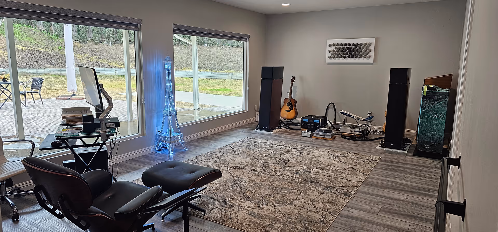Interior music room with guitars, speakers, studio gear, and a large wall of windows.