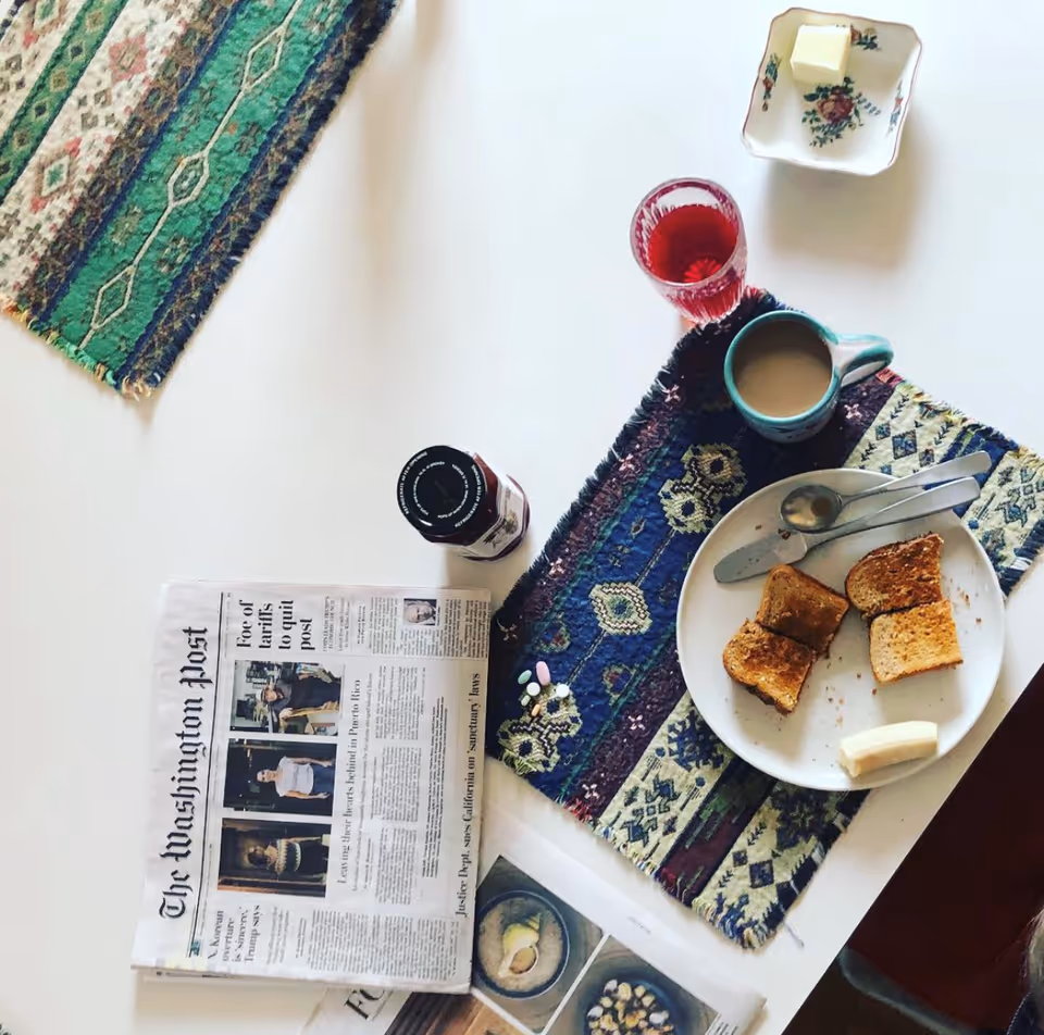 Overhead view of a breakfast setup with toast, coffee, jam, and a newspaper on a table.
