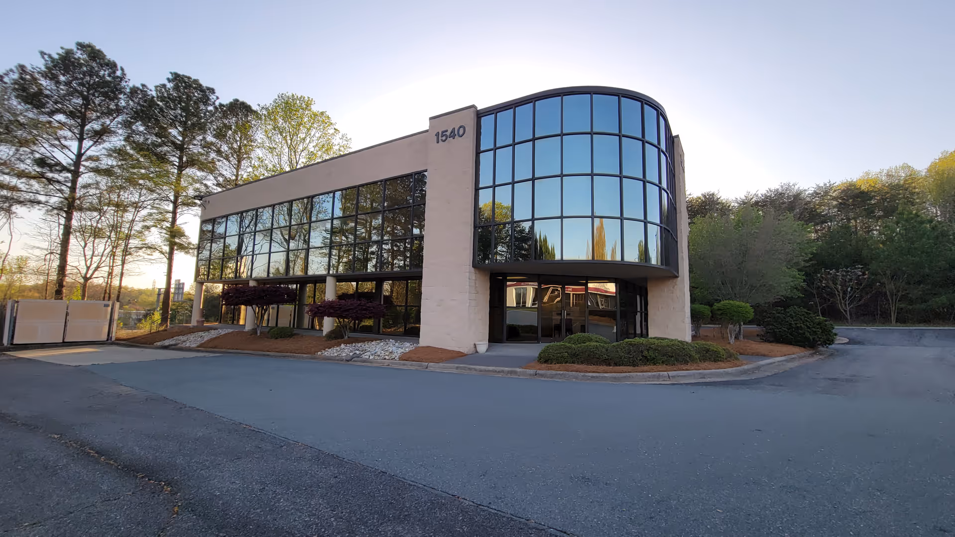 Modern glass-front building with curved facade and surrounding landscaping.