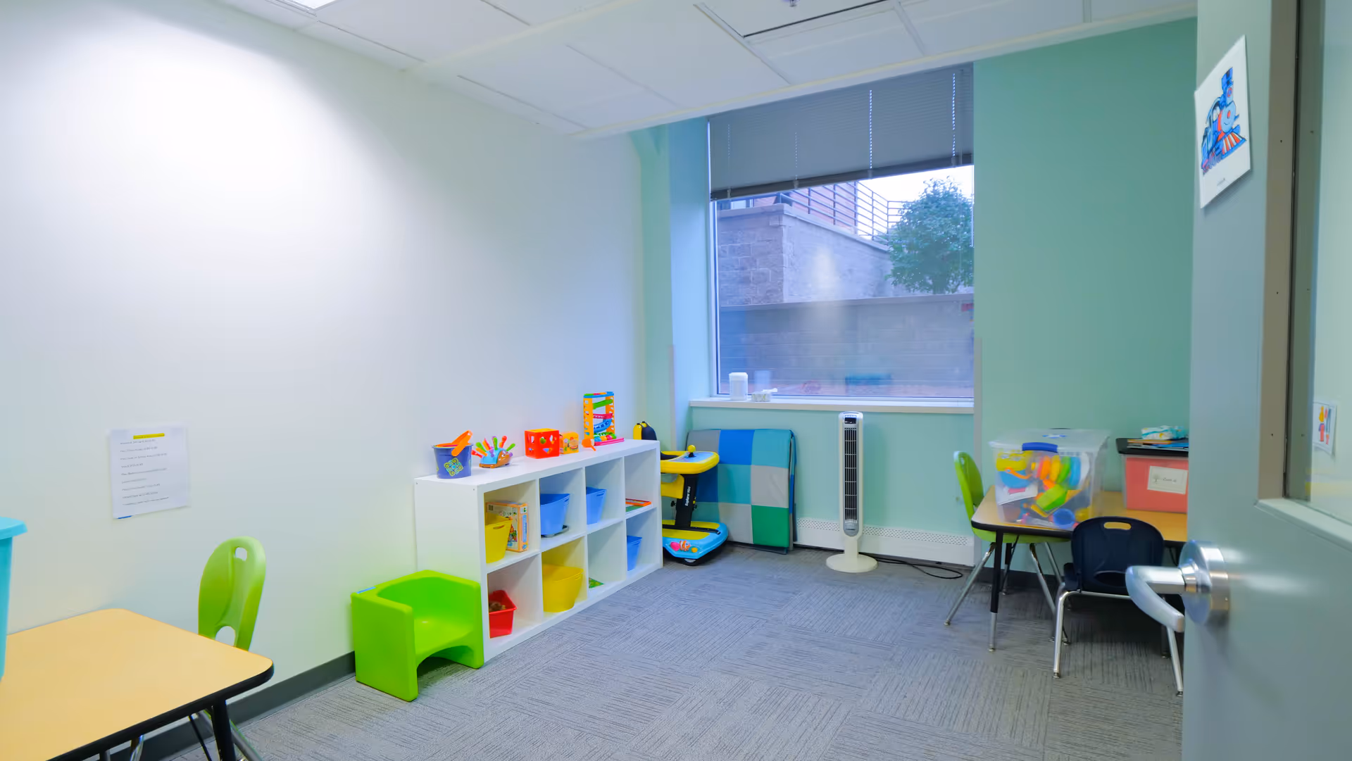 Bright playroom with cubby shelves, colorful toys, and small tables.