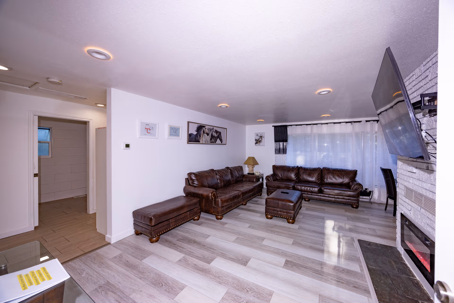 Spacious living room with brown leather sofas, ottoman, fireplace, and mounted TV.
