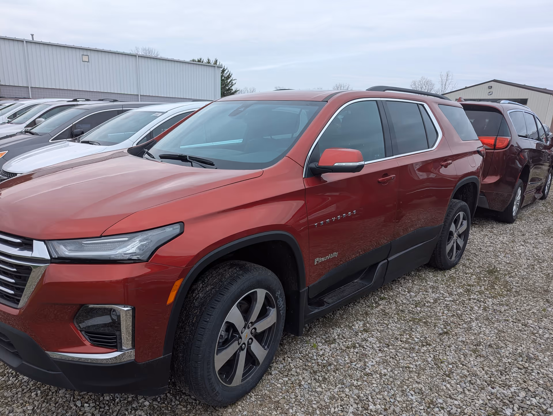 Red SUV parked in a gravel lot with other cars and warehouse buildings.