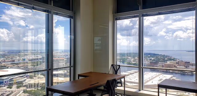 Bright office area with two desks and black chairs overlooking a city skyline.