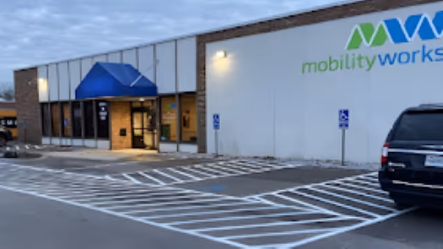Exterior view of a MobilityWorks facility with a blue canopy entrance and handicapped parking.